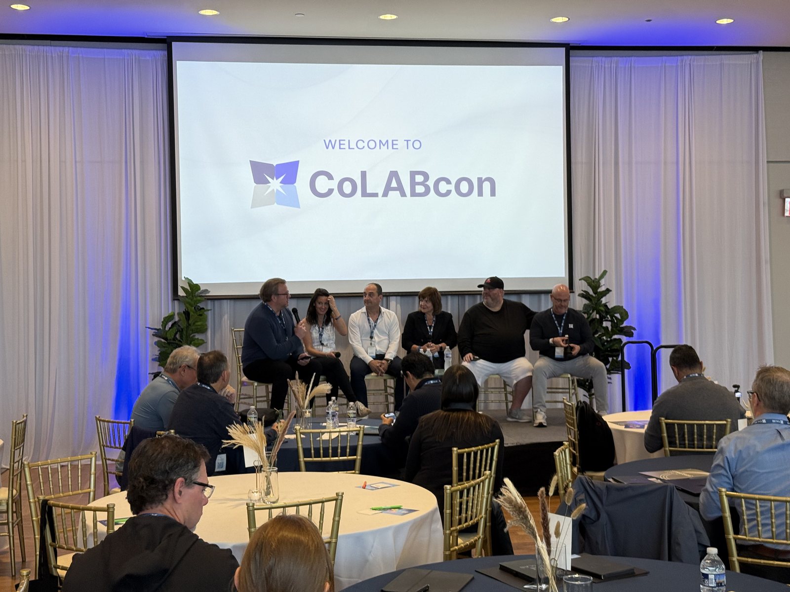 The CoLABcon welcome session — the panel seated in front of the opening slide.