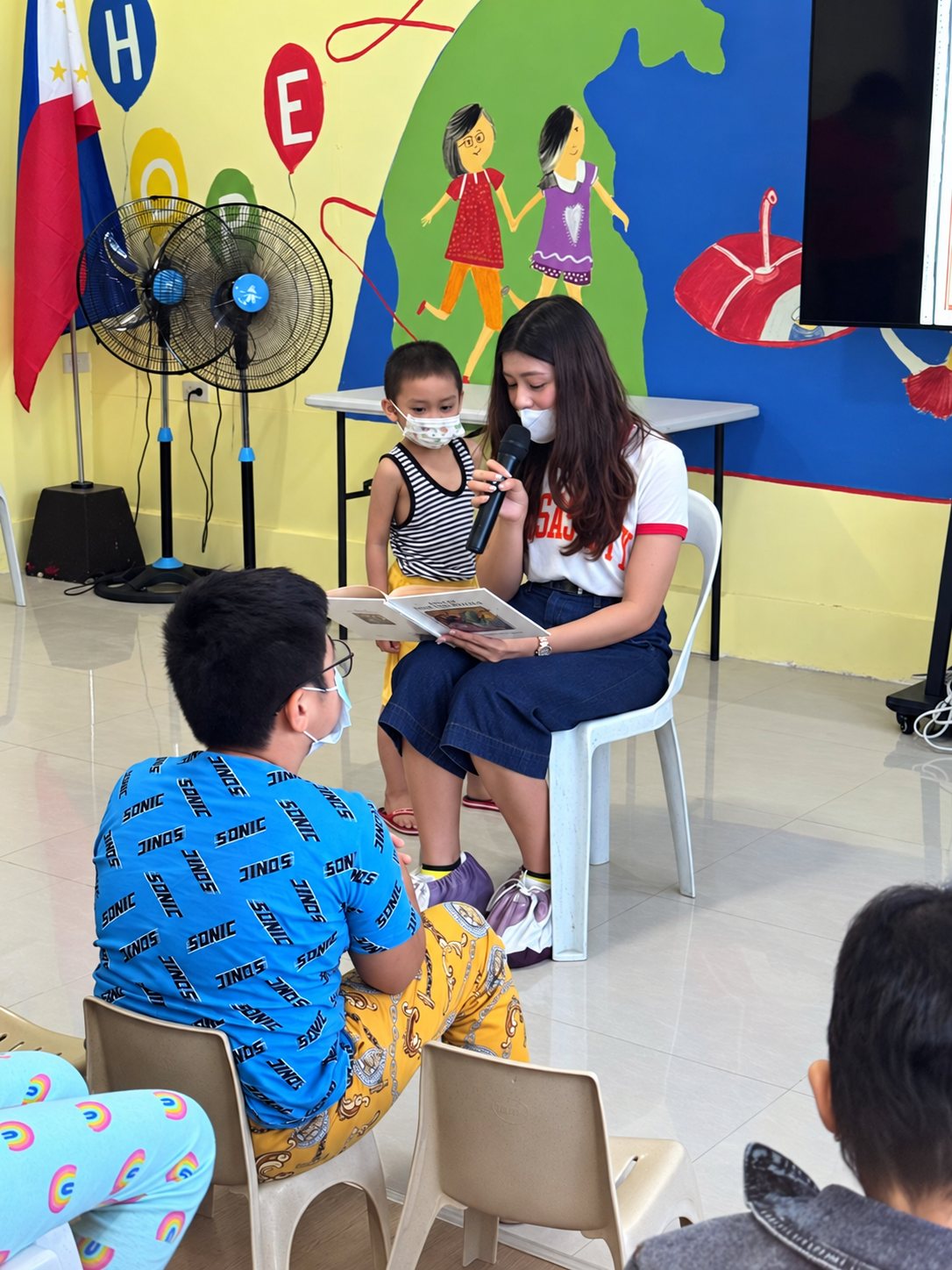 A volunteer reading with children by the mural.